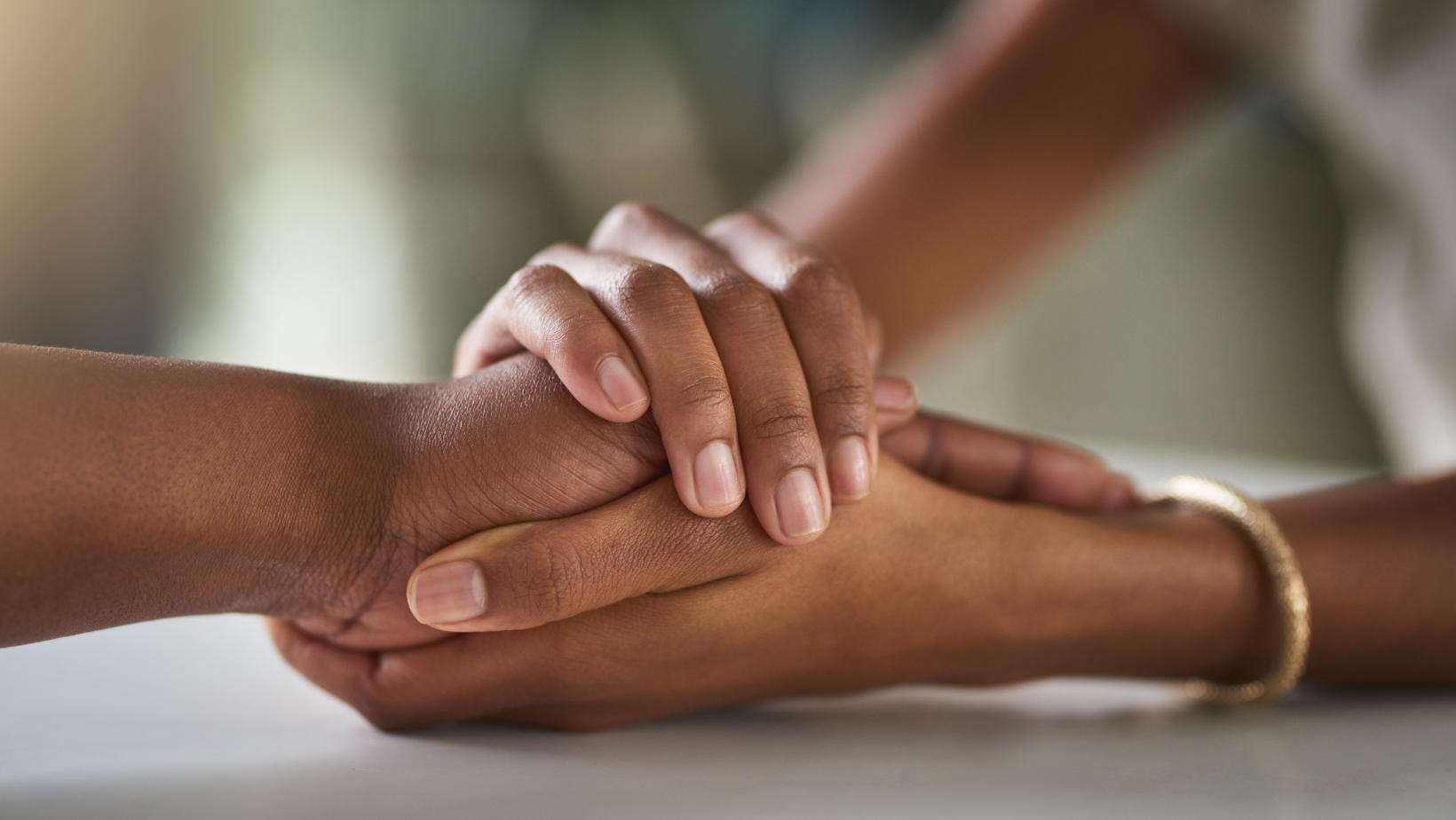 Zdjęcie przedstawia dłonie czarnoskórych ludzi. Dwie dłonie jednej osoby przytrzymują dłoń drugiej osoby. 